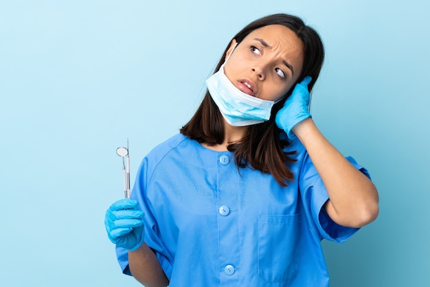 Jovem morena de raça mista dentista segurando ferramentas sobre um fundo isolado frustrada e cobrindo as orelhas