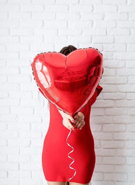 Jovem morena de vestido vermelho segurando um balão de coração vermelho