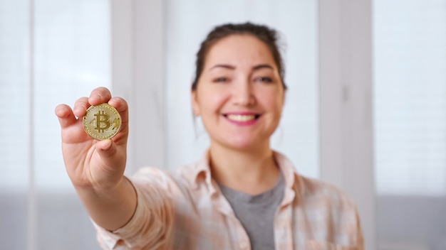 Jovem morena desfocada com bitcoin dourado na mão, foco seletivo