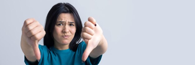 Jovem morena em uma blusa azul dando o polegar para baixo gesto olhando com expressão negativa