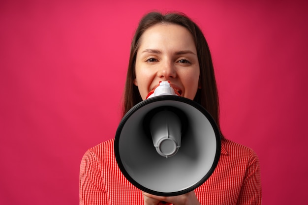 Jovem morena gritando no megafone contra um fundo rosa