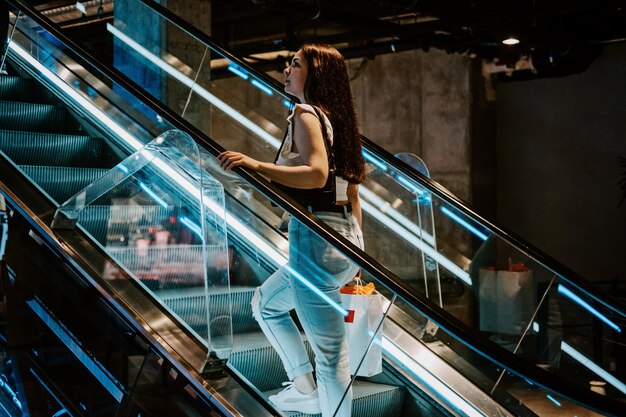 Foto jovem morena latina mulher atraente com sacos de compras na escada rolante na loja de moda