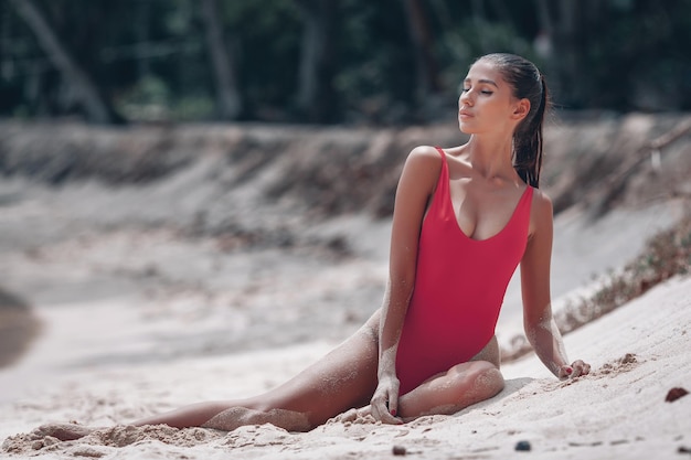 Jovem morena linda em um maiô vermelho tomando sol na areia na praia na Tailândia em Phuket