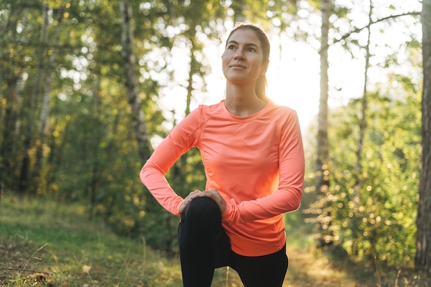 Jovem morena magra em roupas esportivas fazendo alongamento na floresta na hora dourada do nascer do sol saúde e bem-estar estilo de vida fitness