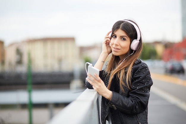 Jovem morena ouvindo música por fones de ouvido em ambiente urbano