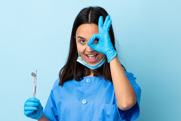 Jovem morena raça mista dentista mulher segurando ferramentas mostrando sinal ok com os dedos