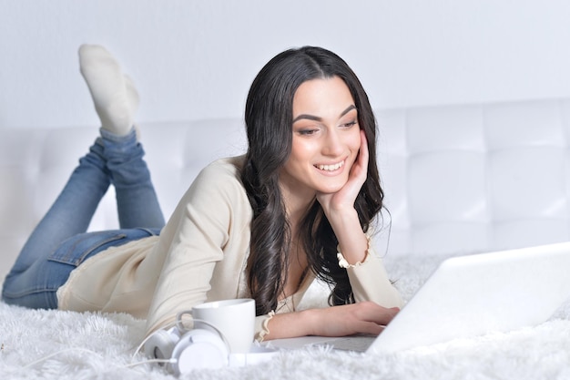 Jovem morena relaxando na cama, usando laptop