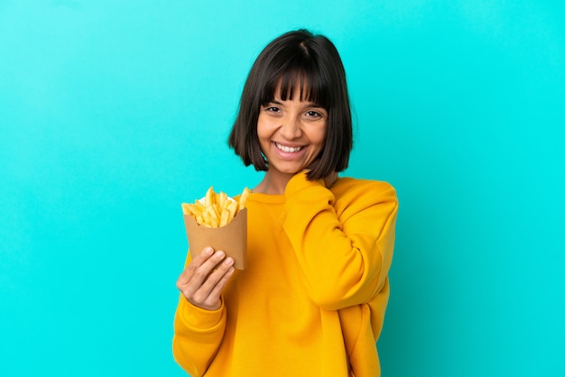 Jovem morena segurando batatas fritas sobre um fundo azul isolado rindo