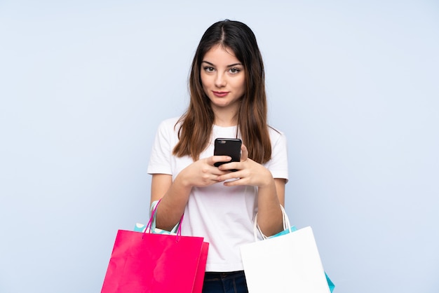 Jovem morena segurando sacolas de compras e escrever uma mensagem com o celular para um amigo