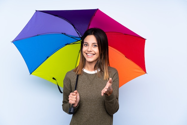 Jovem morena segurando um guarda-chuva sobre parede azul aperto de mão depois de um bom negócio
