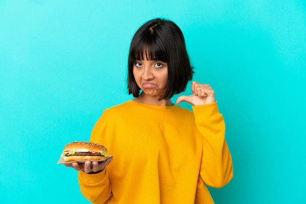 Foto jovem morena segurando um hambúrguer sobre um fundo isolado, orgulhosa e satisfeita