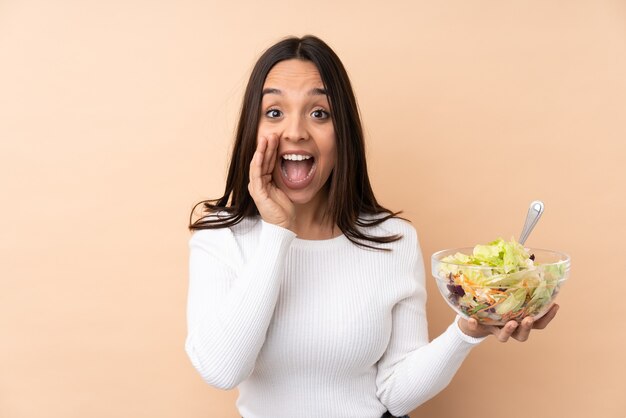 Jovem morena segurando uma salada sobre um fundo isolado e gritando com a boca bem aberta