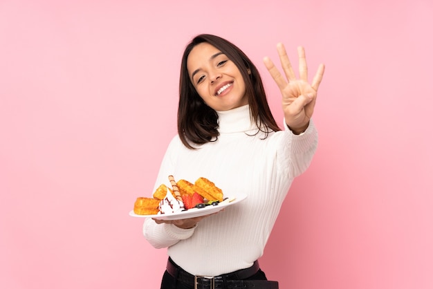 Jovem morena segurando waffles em uma rosa isolada feliz e contando quatro com os dedos