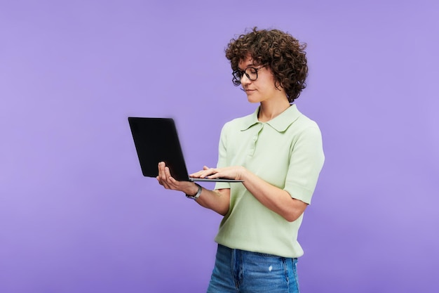 Jovem morena séria em roupas casuais digitando no teclado do laptop