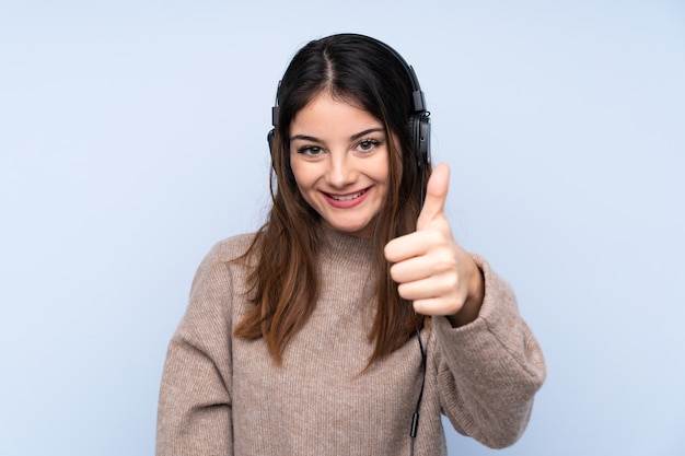 Jovem morena sobre música de parede azul isolado e com o polegar para cima