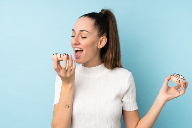 Jovem morena sobre parede azul isolada, comendo um donut