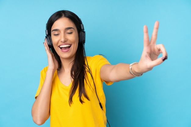 Jovem morena sobre parede azul isolada, ouvir música e cantar