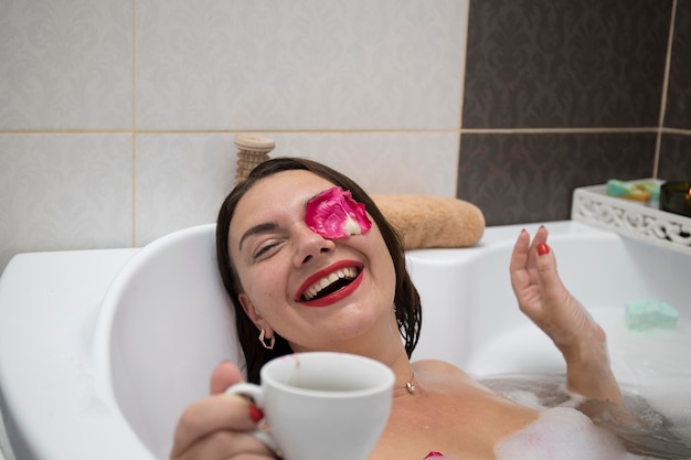 Foto jovem morena sorridente tomando banho com pétalas de rosa em casa fazendo tratamentos de spa para equilíbrio e saúde mental