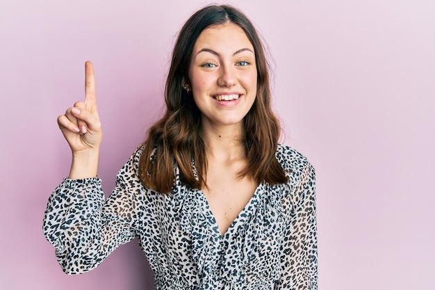 Jovem morena vestindo elegante camisa animal print sorrindo com uma ideia ou pergunta apontando o dedo para cima com cara feliz, número um