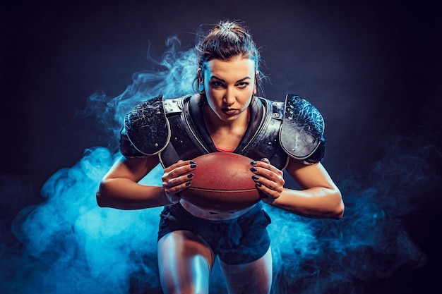 Jovem morena vestindo uniforme sexy de jogador de futebol de rugby posando com bola.