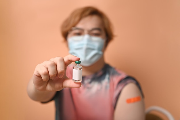 Jovem mostrando garrafa de vacina e braço com curativo após injeção de vacina