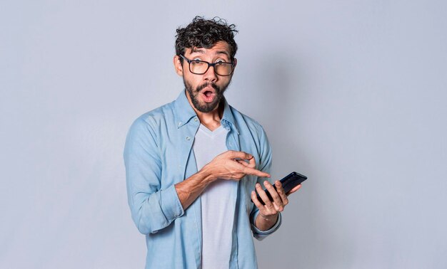 Jovem mostrando o conceito de tela do celular em branco de homem chocado apontando para seu celular