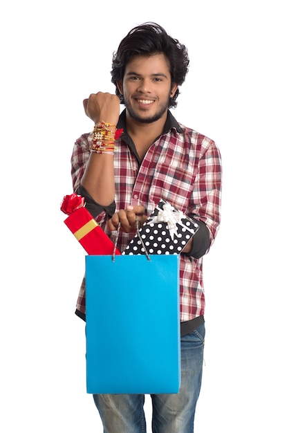 Jovem mostrando rakhi na mão com sacolas de compras e caixa de presente por ocasião do festival raksha bandhan.