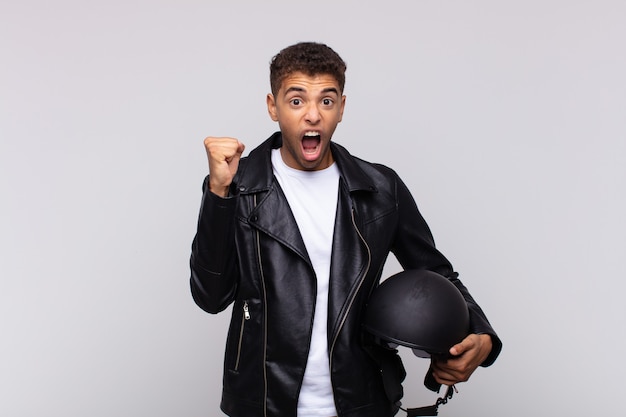 Jovem motociclista gritando agressivamente com uma expressão de raiva ou com os punhos cerrados celebrando o sucesso