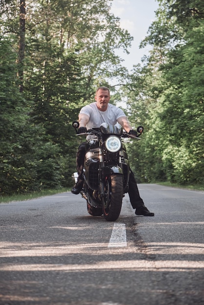 Foto jovem motociclista masculino viaja de moto sozinho em uma estrada de asfalto na floresta