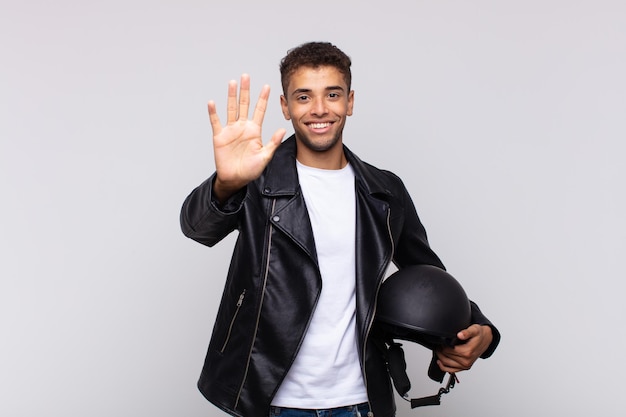 Jovem motociclista sorrindo e parecendo amigável, mostrando o número cinco ou quinto com a mão para a frente, em contagem regressiva