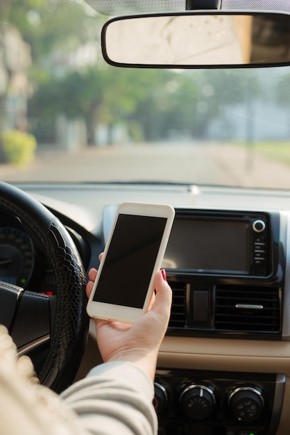 Jovem motorista do sexo feminino usando smartphone com tela de toque e mão segurando o volante de um carro.