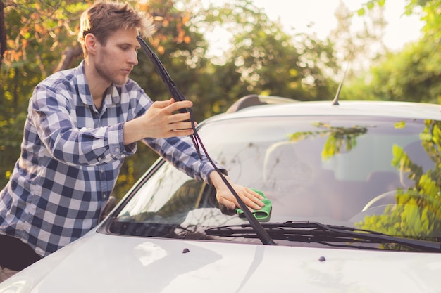 Jovem motorista do sexo masculino limpa seu carro ao ar livre em dias de verão