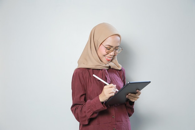 Jovem muçulmana asiática com confiança usando óculos e usando tablet sobre