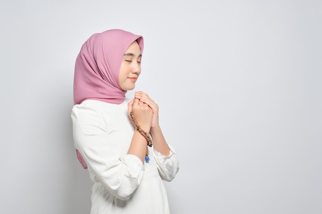 Jovem muçulmana asiática orando a Deus com tasbih isolado sobre fundo branco