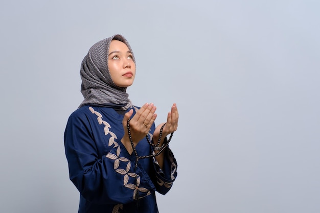 Jovem muçulmana asiática orando a Deus com tasbih isolado sobre fundo branco