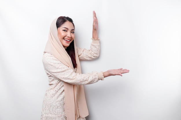 Jovem muçulmana asiática sorrindo enquanto aponta para copiar o espaço ao lado dela