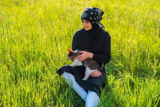 Jovem muçulmana brincando com gato no parque verde na grama