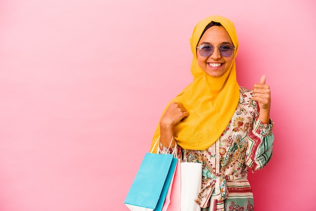 Jovem muçulmana comprando roupas isoladas em uma parede rosa sorrindo e levantando o polegar