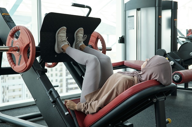 Jovem muçulmana empurrando parte do equipamento esportivo enquanto faz exercícios difíceis na academia