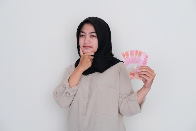 Jovem muçulmana mostrando expressão de pensamento enquanto segura o dinheiro