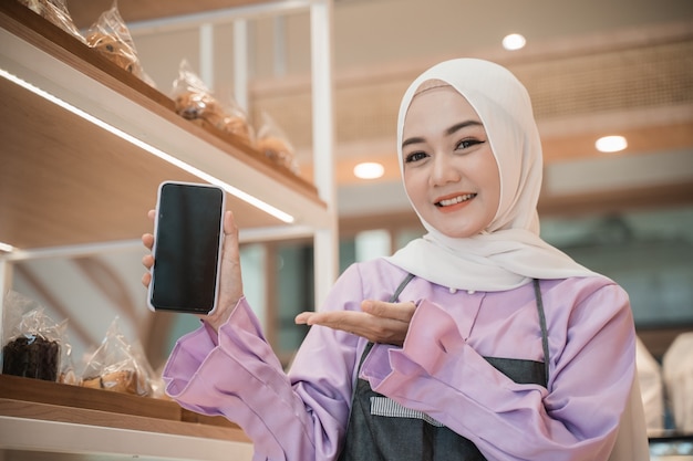 Jovem muçulmana sorridente com hijab mostrando a tela do celular para a câmera