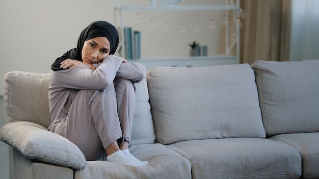 Jovem muçulmana triste e triste sozinha senta-se no sofá problema de saúde gravidez divórcio menina islâmica em hijab