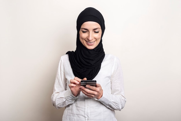 Jovem muçulmana usando hijab segurando um telefone nas mãos e sorrindo