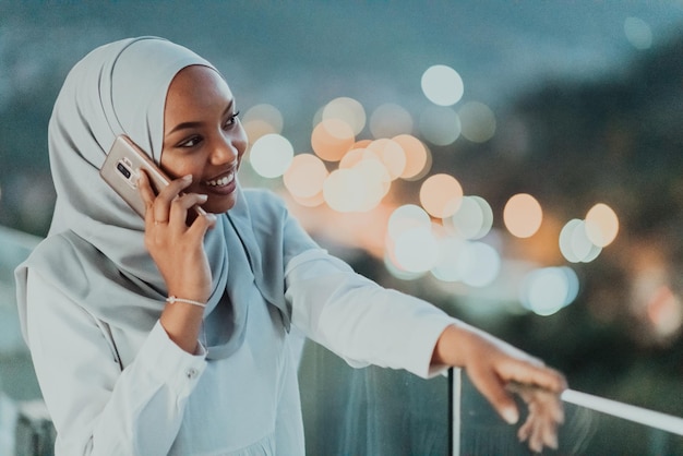 Jovem muçulmana usando véu de cachecol na rua urbana da cidade à noite enviando mensagens de texto em um smartphone com luz da cidade bokeh ao fundo. Foto de alta qualidade