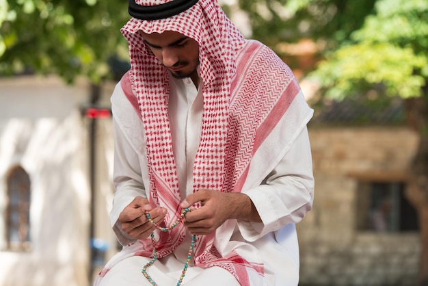 Jovem muçulmano fazendo oração tradicional a Deus enquanto usava um boné tradicional Dishdasha