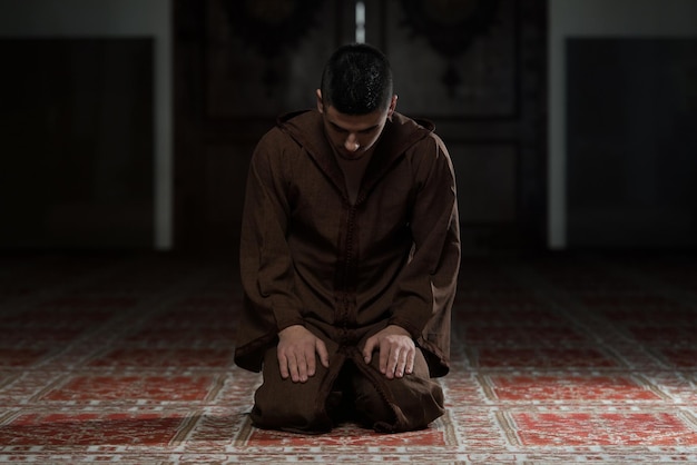 Jovem muçulmano fazendo oração tradicional a Deus enquanto usava um boné tradicional Djellaba