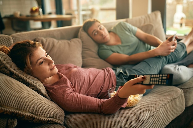 Jovem mudando de canal na TV enquanto relaxa no sofá com o namorado