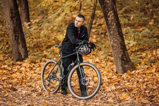 Jovem muito atlético em pé com bicicleta no parque outono