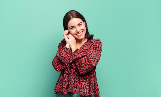 Jovem, muito casual, se sentindo apaixonada e bonita, adorável e feliz, sorrindo romanticamente com as mãos ao lado do rosto