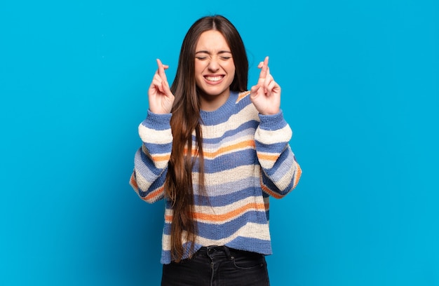 Jovem, muito casual, sentindo-se nervosa e esperançosa, cruzando os dedos, rezando e esperando por boa sorte